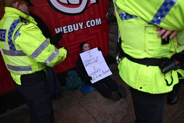 Police officers talk to a protester holding a placard reading 'I oppose genocide, I support Palestine Action' during a demonstration in support of "Defend Our Juries" and their campaign against the ban on Palestine Action, in Leeds, northern England, on November 18, 2025. (Photo by Paul ELLIS / AFP)