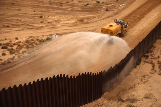 This aerial view shows a construction vehicle spraying water along the secondary border wall built between Santa Teresa, New Mexico, United States and Ciudad Juarez, Chihuahua, Mexico on November 18, 2025. (Photo by HERIKA MARTINEZ / AFP)