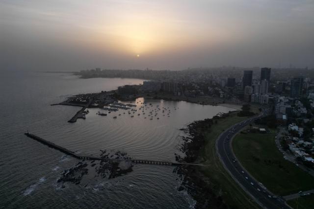 Aerial view of a dust cloud originated in the Argentinian Patagonia seen during sunset in Montevideo on November 18, 2025. A "large dust cloud" that originated in the Argentinian Patagonia entered Uruguay and will affect visibility in coastal areas at least until the early hours of November 19, according to the meteorological authority. The strong wind gusts affecting Patagonia caused "a large dust cloud," generated by the suspension of fine particulate matter in the air, which entered through the Rio de la Plata, the Uruguayan Institute of Meteorology (Inumet) reported. (Photo by Mariana SUAREZ / AFP)