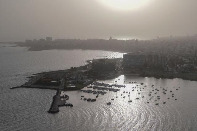 Aerial view of a dust cloud originated in the Chilean-Argentinian Patagonia seen during sunset in Montevideo on November 18, 2025. A "large dust cloud" that originated in the Patagonia entered Uruguay and will affect visibility in coastal areas at least until the early hours of November 19, according to the meteorological authority. The strong wind gusts affecting Patagonia caused "a large dust cloud," generated by the suspension of fine particulate matter in the air, which entered through the Rio de la Plata, the Uruguayan Institute of Meteorology (Inumet) reported. (Photo by Mariana SUAREZ / AFP)