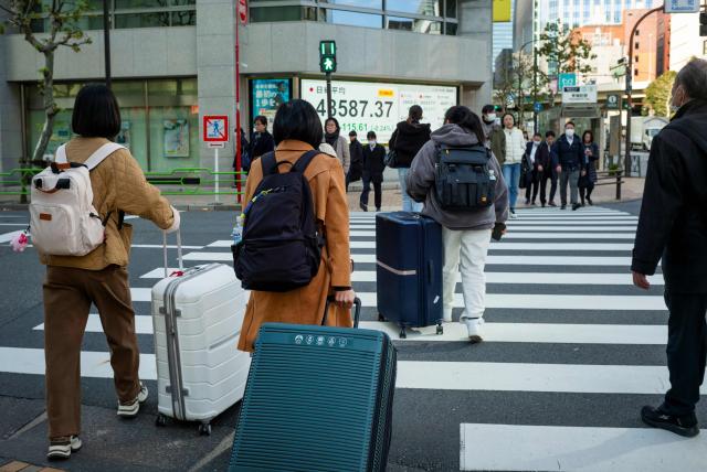 Pedestrians cross a road with their travel suitcases in Tokyo on November 19, 2025. (Photo by Kazuhiro NOGI / AFP)