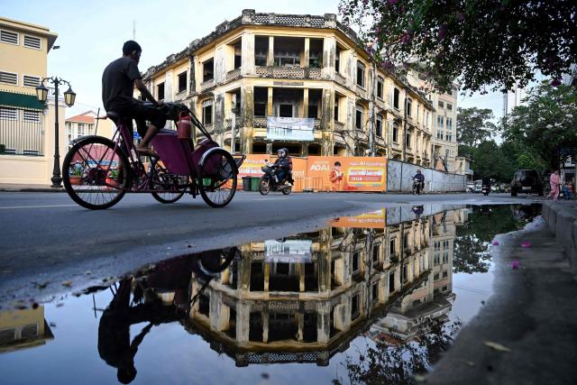 A man rides his cyclo in front of an old building in Phnom Penh on November 19, 2025. (Photo by TANG CHHIN Sothy / AFP)
