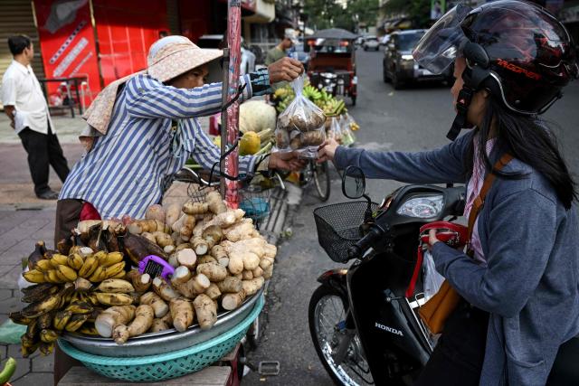 A woman (R) buys red arrow root along a street in Phnom Penh on November 19, 2025. (Photo by TANG CHHIN Sothy / AFP)