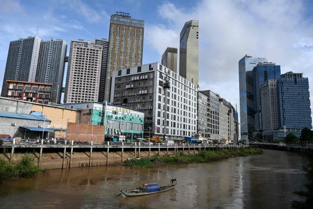 A fisherman rows his boat along a canal in front of high-rise buildings in Phnom Penh on November 19, 2025. (Photo by TANG CHHIN Sothy / AFP)