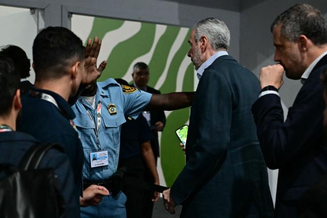 A UN police officer denies access to a room to COP30 President Andre Correa do Lago (2-R) during the COP30 UN Climate Change Conference in Belem, Para State, Brazil, on November 19, 2025. COP30 host Brazil pushed Tuesday for an early breakthrough at UN climate talks, with nations weighing a proposed deal that seeks to bridge major differences on fossil fuels, finance and trade barriers. Brazil wants an agreement reached by midweek, with President Luiz Inacio Lula da Silva to make an unexpected return on Wednesday to Belem, the host city in the country's Amazon region, in a high-level bid to seal a deal. (Photo by Pablo PORCIUNCULA / AFP)