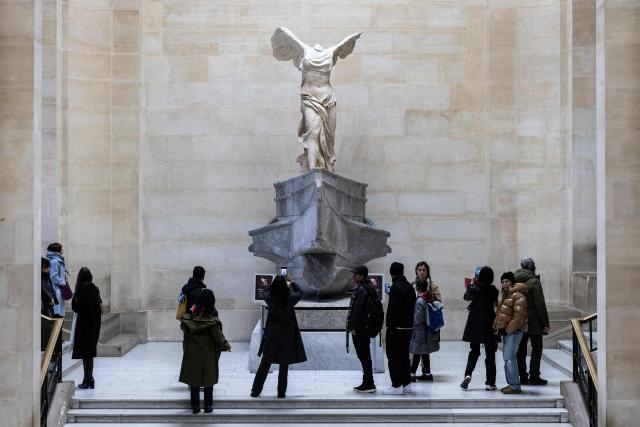 Visitors look at the Greek sculpture 'Winged Victory of Samothrace' at the Louvre Museum in Paris on November 19, 2025. (Photo by Sébastien DUPUY / AFP)
