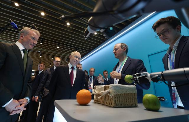 In this pool photograph distributed by the Russian state agency Sputnik, Russia's President Vladimir Putin, accompanied by Sberbank's CEO German Gref, visits an exhibition of the AI Journey international AI (Artificial intelligence) conference in Moscow on November 19, 2025. Russia's anthropomorphic AI-equipped robot developed by technology company Sber was presented to the Russian leader. (Photo by Vyacheslav PROKOFYEV / POOL / AFP)
