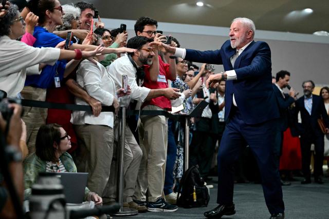 Brazil's President Luiz Inacio Lula da Silva (R) greets journalists before a press conference during the COP30 UN Climate Change Conference in Belem, Para state, Brazil, on November 19, 2025. Brazilian President Luiz Inacio Lula da Silva hit the corridors of COP30 in Belem on Wednesday, in a push to land a deal at the UN climate talks as nations remained divided over contentious issues. (Photo by Pablo PORCIUNCULA / AFP)