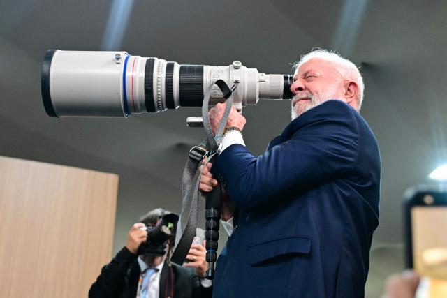 Brazil's President Luiz Inacio Lula da Silva looks through a camera lens before a press conference during the COP30 UN Climate Change Conference in Belem, Para state, Brazil, on November 19, 2025. Brazilian President Luiz Inacio Lula da Silva hit the corridors of COP30 in Belem on Wednesday, in a push to land a deal at the UN climate talks as nations remained divided over contentious issues. (Photo by Pablo PORCIUNCULA / AFP)