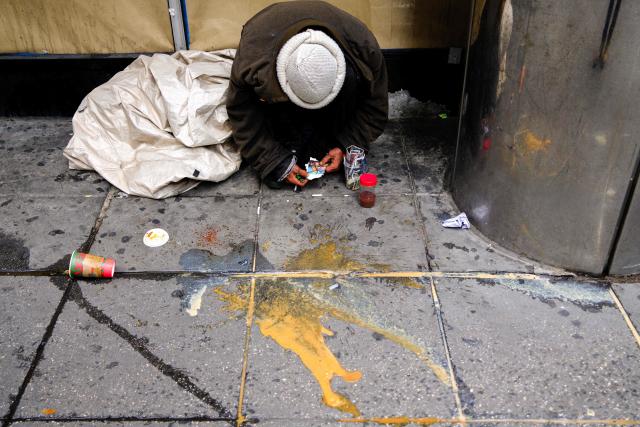 A homeless person crouches while asleep on a sidewalk, clutching a photo in their hands, in Manhattan, New York, on November 19, 2025. (Photo by CHARLY TRIBALLEAU / AFP)