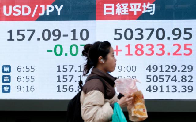 A woman walks past an electronic quotation boards displaying numbers of the Nikkei Stock Average on the Tokyo Stock Exchange (R) and the foreign exchange rate of the US dollar against the Japanese yen (L) during a morning session in Tokyo on November 20, 2025. (Photo by Kazuhiro NOGI / AFP)