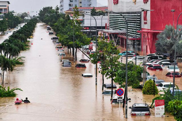 People (L) wade through floodwaters near inundated vehicles in Nha Trang, Vietnam's coastal province of Khanh Hoa on November 20, 2025. The death toll from a week of torrential rain that triggered floods and landslides in central Vietnam has risen to 16 while thousands of homes inundated in "historic" floodings, authorities said. (Photo by Duc Thao / AFP)