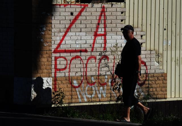 (FILES) A man walks down a street past a wall with the inscription "For Russia" in the Russian-controlled Azov Sea port city of Mariupol in southeastern Ukraine on July 15, 2025, amid the ongoing Russian-Ukrainian conflict. (Photo by Olga MALTSEVA / AFP)