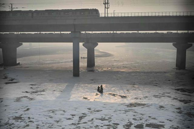 A fisherman rows his boat in the waters of river Yamuna laden with polluted foam, on a smoggy morning in New Delhi November 20, 2025. New Delhi with its sprawling metropolitan region of 30 million residents is regularly ranked among the world's most polluted capitals. Acrid smog blankets the skyline each winter, when cooler air traps pollutants close to the ground, creating a deadly mix of emissions from crop burning, factories and heavy traffic. (Photo by Arun SANKAR / AFP)