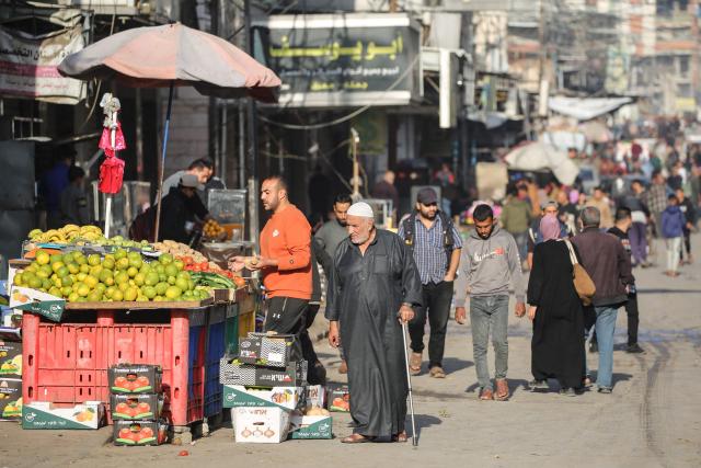 Palestinians walk through a market street in Deir al-Balah, in the central Gaza Strip, on November 20, 2025. The United Nations Security Council voted on November 17 in favour of a US-drafted resolution bolstering the US president's plan for the Gaza Strip -- which has allowed a fragile ceasefire to hold between Israel and Hamas since October 10. (Photo by Eyad Baba / AFP)
