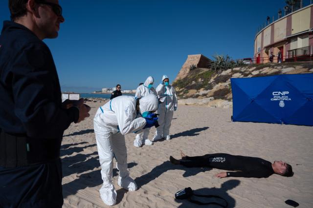 A forensic police officer takes photographs of a participant lying on the beach during the Respuesta25 tsunami drill in Cadiz, on November 20, 2025. Around 20,000 persons took part in the 'Respuesta25' simulation, aimed at assessing institutional coordination, evacuation times and the effectiveness of warning systems before a tidal wave. (Photo by Jorge GUERRERO / AFP)