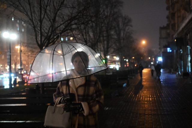 A woman walks under an umbrella along Khreshchatyk Street in Kyiv on November 20, 2025, amid the Russian invasion of Ukraine. (Photo by Sergei GAPON / AFP)