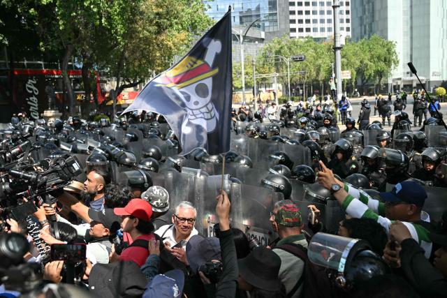 A protester holds a flag bearing the logo of the popular Japanese manga One Piece, a symbol adopted by Gen Z protest movements worldwide, in front of a police cordon across Reforma Avenue during a rally by young Mexicans linked to a global wave of Generation Z protests against the government of Mexico's President Claudia Sheinbaum, in Mexico City, on November 20, 2025. (Photo by Yuri CORTEZ / AFP)