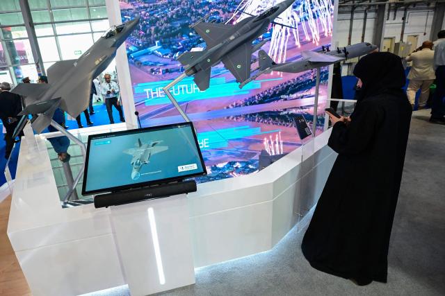 A visitor stands next to models of aircraft displayed at Al-Maktoum International Airport during the Dubai Airshow 2025 in Dubai on November 20, 2025. (Photo by Giuseppe CACACE / AFP)