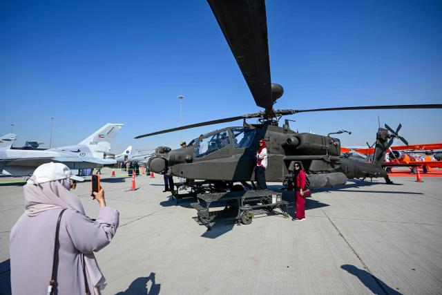 Visitors take photos next to an Apache AH64E displayed at Al-Maktoum International Airport during the Dubai Airshow 2025 in Dubai on November 20, 2025. (Photo by Giuseppe CACACE / AFP)