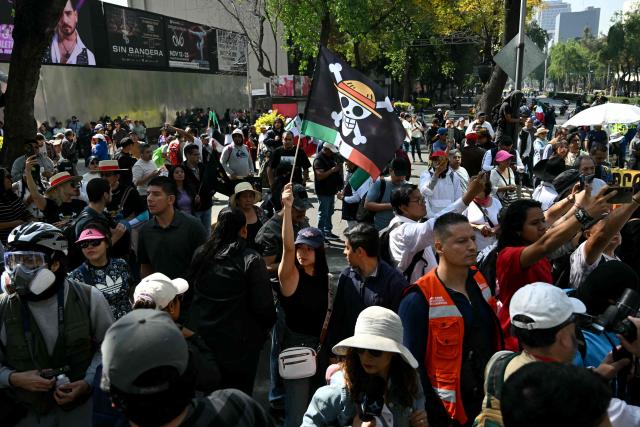A protester holds a flag bearing the logo of the popular Japanese manga One Piece, a symbol adopted by Gen Z protest movements worldwide, during in a rally called by Generation Z against the government of Mexico's President Claudia Sheinbaum, along Reforma Avenue in Mexico City on November 20, 2025. This is the second demonstration called by Generation Z to protest against the leftist government's security policy, after another protest on Saturday ended with more than 100 injured, most of them police officers, and 19 arrested. (Photo by Yuri CORTEZ / AFP)