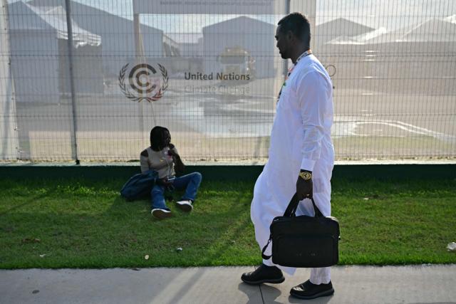 A man walks past a woman sitting outside the COP30 UN Climate Change Conference in Belem, Para state, Brazil, on November 20, 2025, after a fire broke out in a pavilion. A fire erupted at a pavilion inside the venue of the UN's climate talks in Brazil on Thursday, prompting panicked delegates to run for the exits, AFP journalists said. Emergency crews rushed to try to put out the blaze as smoke engulfed the corridor. (Photo by Pablo PORCIUNCULA / AFP)