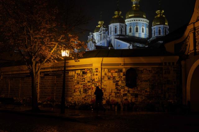 A man walks by the Wall of Remembrance of the Fallen for Ukraine, a memorial dedicated to Ukrainian soldiers during blackout hours in Kyiv on November 20, 2025, following Russian missile and drone attacks on Ukrainian energy infrastructure amid the Russian invasion of Ukraine. (Photo by Tetiana DZHAFAROVA / AFP)