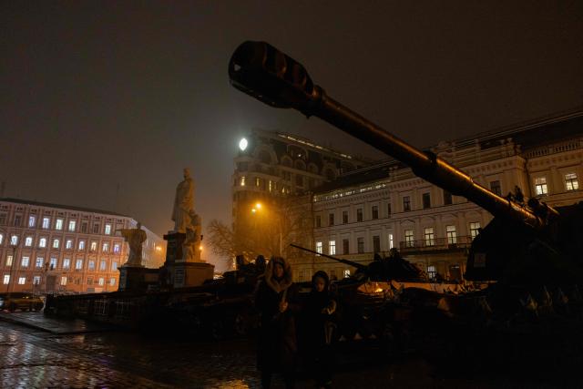 A woman with a child walk through an open-air exhibition of destroyed Russian military vehicles on Mykhailivska Square during blackout hours in Kyiv on November 20, 2025, following Russian missile and drone attacks on Ukrainian energy infrastructure amid the Russian invasion of Ukraine. (Photo by Tetiana DZHAFAROVA / AFP)