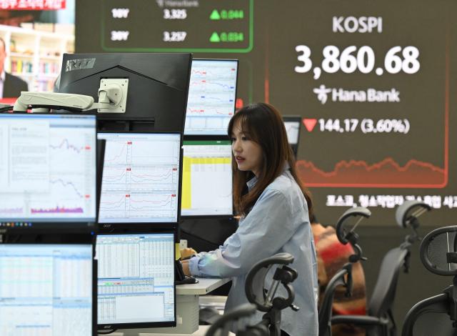 A currency dealer monitors exchange rates as a screen shows South Korea's benchmark stock index (R) in a foreign exchange dealing room at the Hana Bank headquarters in Seoul on November 21, 2025. Japanese and South Korean tech stocks plummeted on November 21, with tech investor SoftBank plunging more than 10 percent as fears over an AI bubble weigh on the market. (Photo by Jung Yeon-je / AFP)