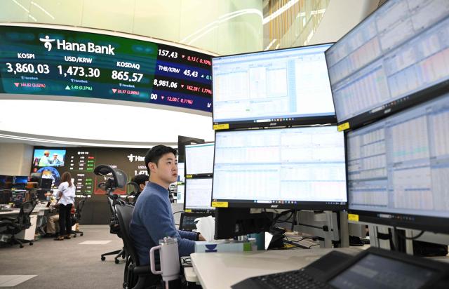 Currency dealers monitor exchange rates as a screen shows South Korea's benchmark stock index (L top) and the Korean won/USD exchange rate (2nd L top) in a foreign exchange dealing room at the Hana Bank headquarters in Seoul on November 21, 2025. Japanese and South Korean tech stocks plummeted on November 21, with tech investor SoftBank plunging more than 10 percent as fears over an AI bubble weigh on the market. (Photo by Jung Yeon-je / AFP)
