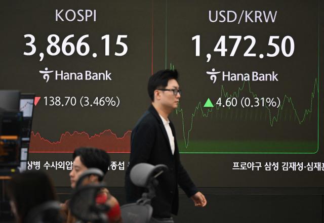 A currency dealer walks past a screen showing South Korea's benchmark stock index (L) and the Korean won/USD exchange rate (R) in a foreign exchange dealing room at the Hana Bank headquarters in Seoul on November 21, 2025. Japanese and South Korean tech stocks plummeted on November 21, with tech investor SoftBank plunging more than 10 percent as fears over an AI bubble weigh on the market. (Photo by Jung Yeon-je / AFP)