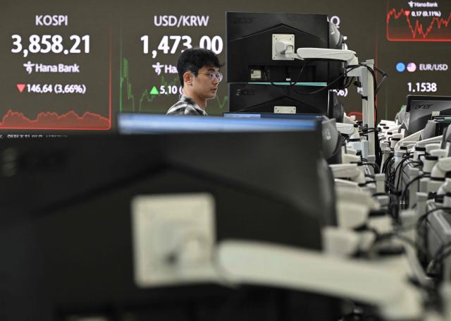 A currency dealer monitors exchange rates as a screen shows South Korea's benchmark stock index (L) and the Korean won/USD exchange rate (C back) in a foreign exchange dealing room at the Hana Bank headquarters in Seoul on November 21, 2025. Japanese and South Korean tech stocks plummeted on November 21, with tech investor SoftBank plunging more than 10 percent as fears over an AI bubble weigh on the market. (Photo by Jung Yeon-je / AFP)
