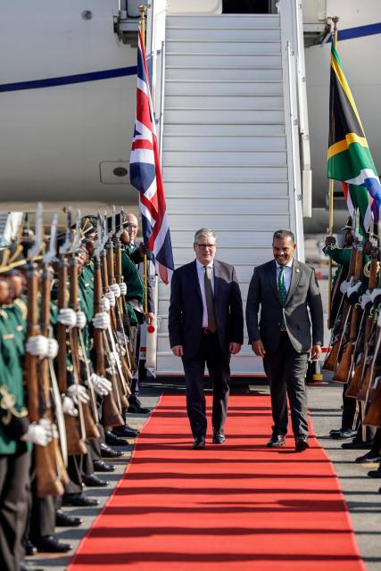 Britain's Prime Minister Keir Starmer (C) is welcomed by a South African representative upon his arrival at at OR Tambo International Airport in Ekurhuleni on November 21, 2025 ahead of the G20 leaders' Summit. (Photo by Marco Longari / POOL / AFP)