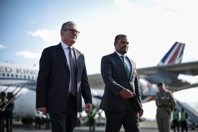 Britain's Prime Minister Keir Starmer (L) is welcomed by a South African official as he arrives at OR Tambo International Airport in Ekurhuleni on November 21, 2025 ahead of the G20 leaders' Summit. (Photo by HENRY NICHOLLS / POOL / AFP)