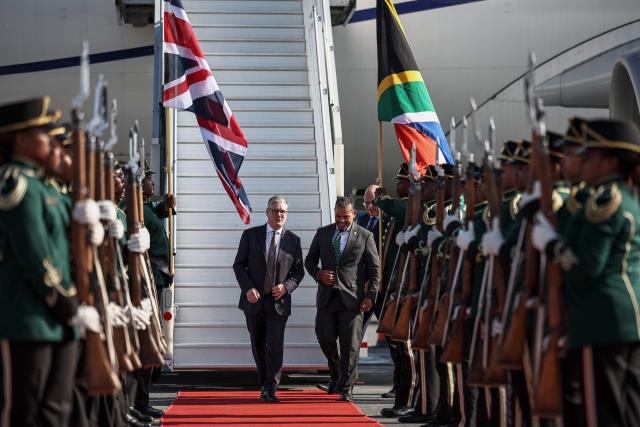 Britain's Prime Minister Keir Starmer (CL) is welcomed by a South African official as he arrives at OR Tambo International Airport in Ekurhuleni on November 21, 2025 ahead of the G20 leaders' Summit. (Photo by HENRY NICHOLLS / POOL / AFP)
