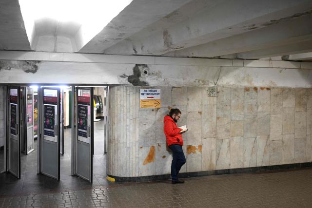 A man reads a book next to the metro entrance in an underground passage in Kyiv on November 21, 2025, amid the Russian invasion of Ukraine. (Photo by Sergei GAPON / AFP)