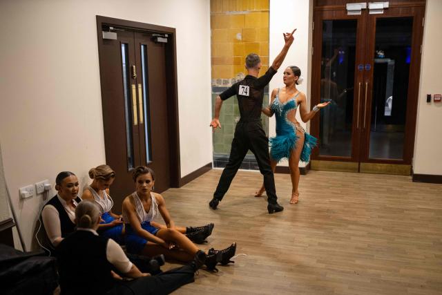 Latin dancing couple Dylan Jones (2nd R) and Hannah Bartholomew (R) practice next to resting dancers before competing in the 'Amateur Under 21 years Latin Championship' of the 50th British National Dance Championships, in the Empress Ballroom of Blackpool's Winter Gardens, in Blackpool, north-west England, on November 20, 2025. The annual, four-day British National Dance Championship features over 2000 entries and showcases 60 hours of competitive dancing, with 23 championship titles in Ballroom and Latin dance disciplines. (Photo by Oli SCARFF / AFP)