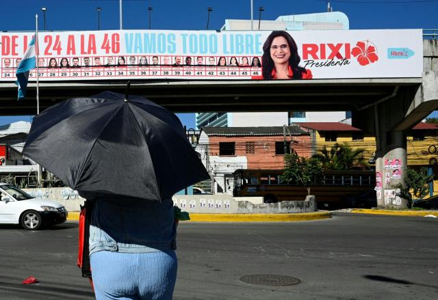 A woman walks past a billboard of presidential candidate Rixi Moncada of the ruling Libertad y Refundacion (LIBRE) party in Tegucigalpa on November 21, 2025. Honduras will hold presidential elections on November 30. (Photo by Orlando SIERRA / AFP)