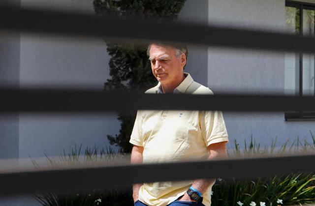 (FILES) Former Brazilian President Jair Bolsonaro gestures from his residence in Brasilia on September 3, 2025. Lawyers for former Brazilian president Jair Bolsonaro on November 21, 2025, requested he be allowed to serve a 27-year prison sentence for coup plotting under house arrest, citing ill health. (Photo by Sergio Lima / AFP)