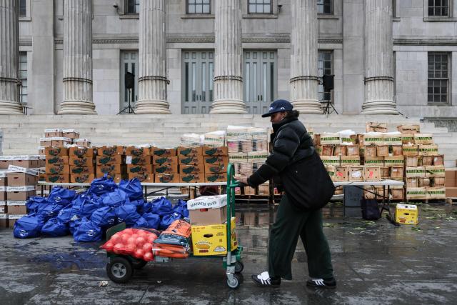 A volunteer pushes a cart loaded with food during a Thanksgiving food distribution event outside of Brooklyn Borough Hall on November 21, 2025 in New York City. Fresh produce, non-perishables and other food items were handed out to 125 Brooklyn houses of worship, community kitchens and other community-based organizations addressing food insecurity and homelessness. (Photo by ANGELA WEISS / AFP)