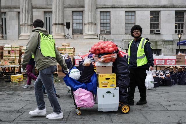 Volunteers move a cart loaded with food during a Thanksgiving food distribution event outside of Brooklyn Borough Hall on November 21, 2025 in New York City. Fresh produce, non-perishables and other food items were handed out to 125 Brooklyn houses of worship, community kitchens and other community-based organizations addressing food insecurity and homelessness. (Photo by ANGELA WEISS / AFP)