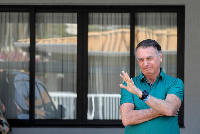 (FILES) Former Brazilian President Jair Bolsonaro waves at his residence in Brasilia on September 11, 2025. Lawyers for former Brazilian president Jair Bolsonaro on November 21, 2025, requested he be allowed to serve a 27-year prison sentence for coup plotting under house arrest, citing ill health. (Photo by Sergio Lima / AFP)