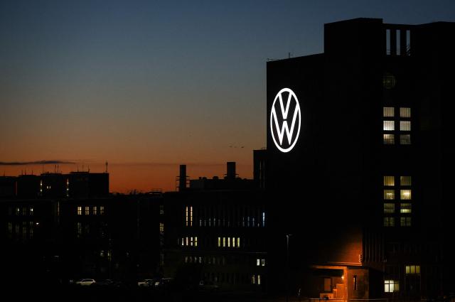 The illuminated VW logo is seen on the power plant building at the headquarters of German carmaker Volkswagen (VW) during sunset in Wolfsburg, central Germany, on November 21, 2025. (Photo by Ronny HARTMANN / AFP)