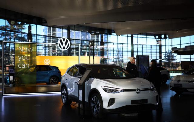 Visitors stand by a ID.4 car in the customer centre at the headquarters of German carmaker Volkswagen (VW) in Wolfsburg, central Germany, on November 21, 2025. (Photo by Ronny HARTMANN / AFP)
