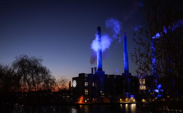 The illuminated VW logo is seen on the power plant building at the headquarters of German carmaker Volkswagen (VW) in Wolfsburg, central Germany, at dusk on November 21, 2025. (Photo by Ronny HARTMANN / AFP)