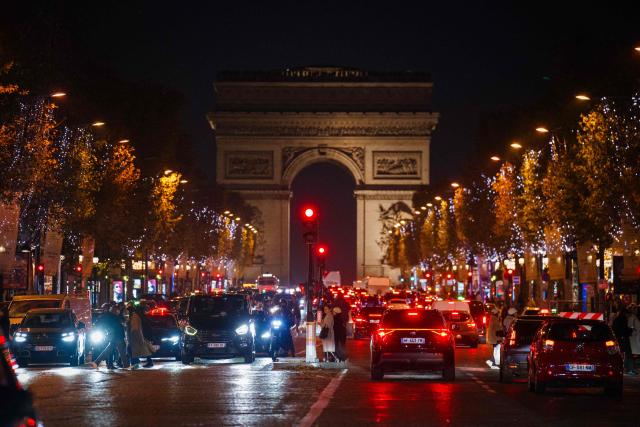 Pedestrians cross the Champs-Elysees Avenue with Christmas illuminations and the Arc de Triomphe in the background, in Paris, on November 21, 2025. (Photo by Dimitar DILKOFF / AFP)