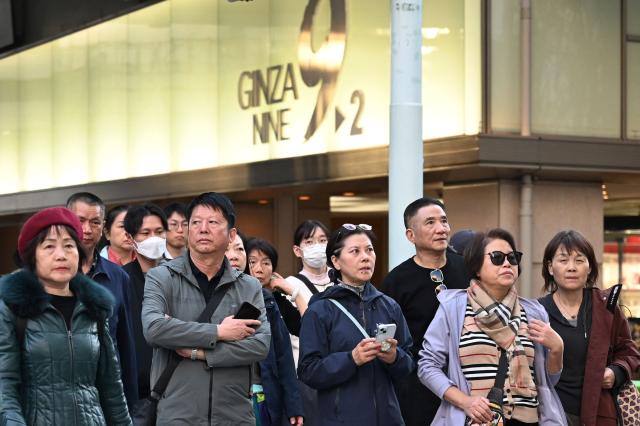 (FILES) Members of a Chinese tour group wait to cross a road in the Ginza shopping district in Tokyo on November 17, 2025. Taiwan lifted all restrictions on Japanese food imports on November 22, in another show of support for Tokyo after reports that China will stop purchases over a row with the new prime minister. (Photo by GREG BAKER / AFP)