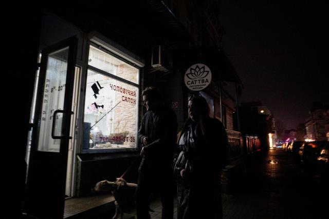 People with a dog walk down a non-illuminated street during blackout hours in Kyiv on November 21, 2025, following Russian missile and drone attacks on Ukrainian energy infrastructure amid the Russian invasion of Ukraine. (Photo by Tetiana DZHAFAROVA / AFP)