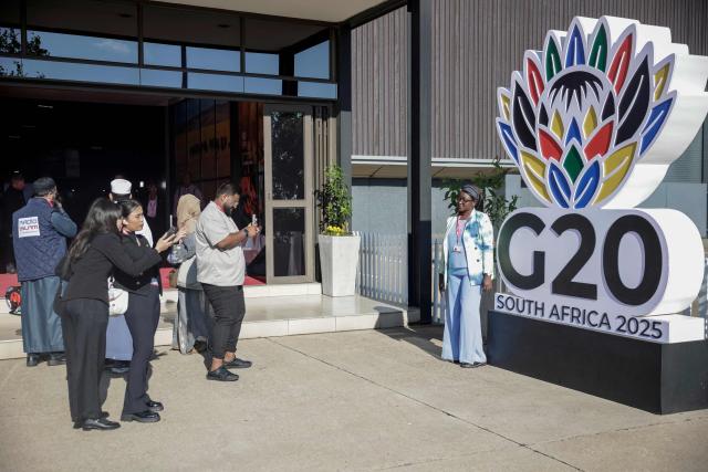 Attendees take pictures next to a G20 logo ahead of the opening of the G20 Leaders' Summit at the Nasrec Expo Centre in Johannesburg on November 22, 2025. (Photo by GIANLUIGI GUERCIA / AFP)
