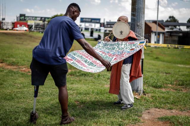 TOPSHOT - A pro-Palestinian protester (L) reads the banner of Japanese Buddhist Monk and Anti-nuclear campaigner Toyoshige Sekiguchi (R) who is protesting next to a road near the Nasrec Expo Centre in Johannesburg on November 22, 2025 ahead of the opening of the G20 Leaders' Summit. (Photo by Marco Longari / AFP)